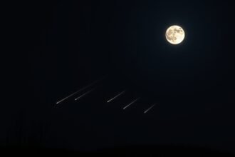 A high-resolution image of a dark sky with a bright full moon and multiple meteors streaking across the horizon, with a few trees or hills in the foreground to give a sense of depth and perspective.