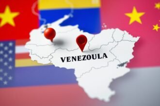 A photo of a map of Venezuela with a red pin marking the capital city Caracas, with a subtle background image of the US, Russian, and Chinese flags.