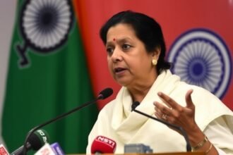 A photo of Mamata Banerjee speaking at a press conference with a background of West Bengal state flag and a faint image of the Election Commission of India logo
