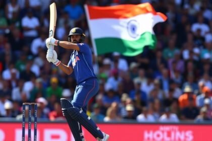 A photo of Virat Kohli batting in the first ODI against New Zealand, with a crowd of spectators in the background and the Indian flag waving high.